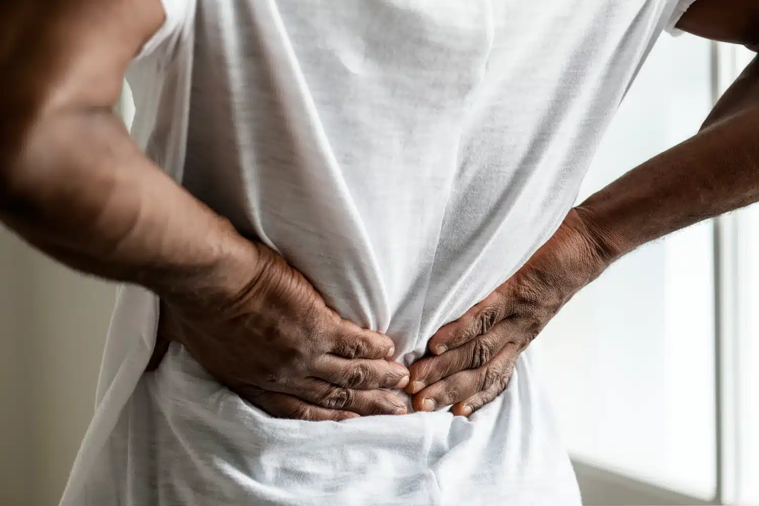personne posant ses mains sur le bas de son dos à travers un t-shirt blanc, illustrant une douleur lombaire