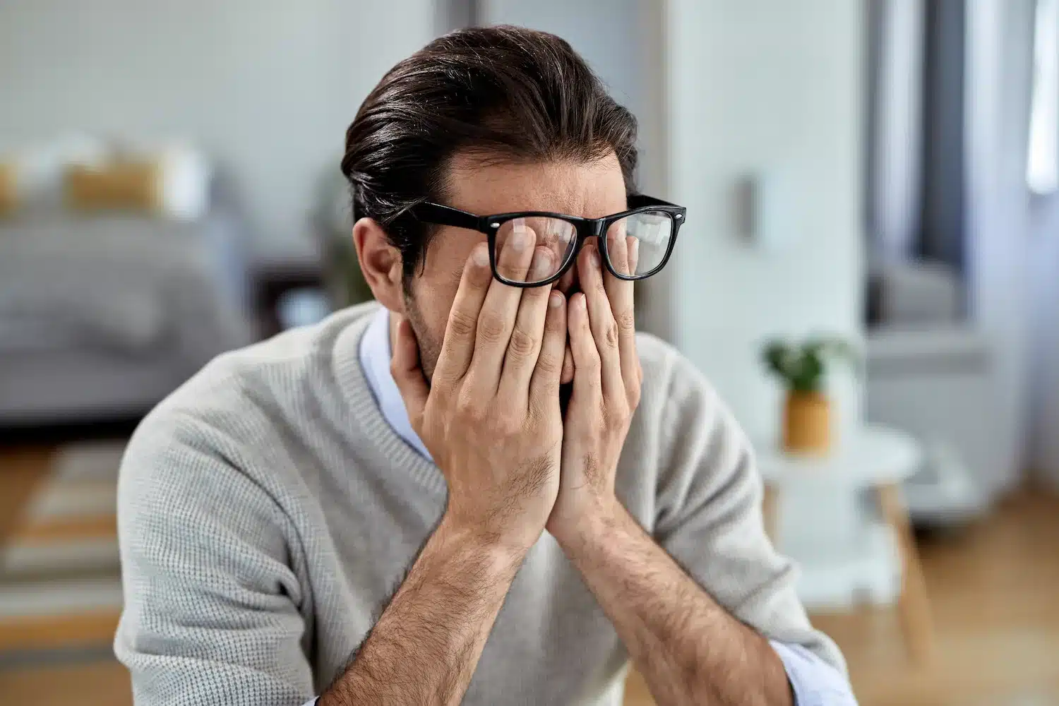homme portant des lunettes assis à l’intérieur, les mains couvrant son visage comme s’il était dépassé ou fatigué