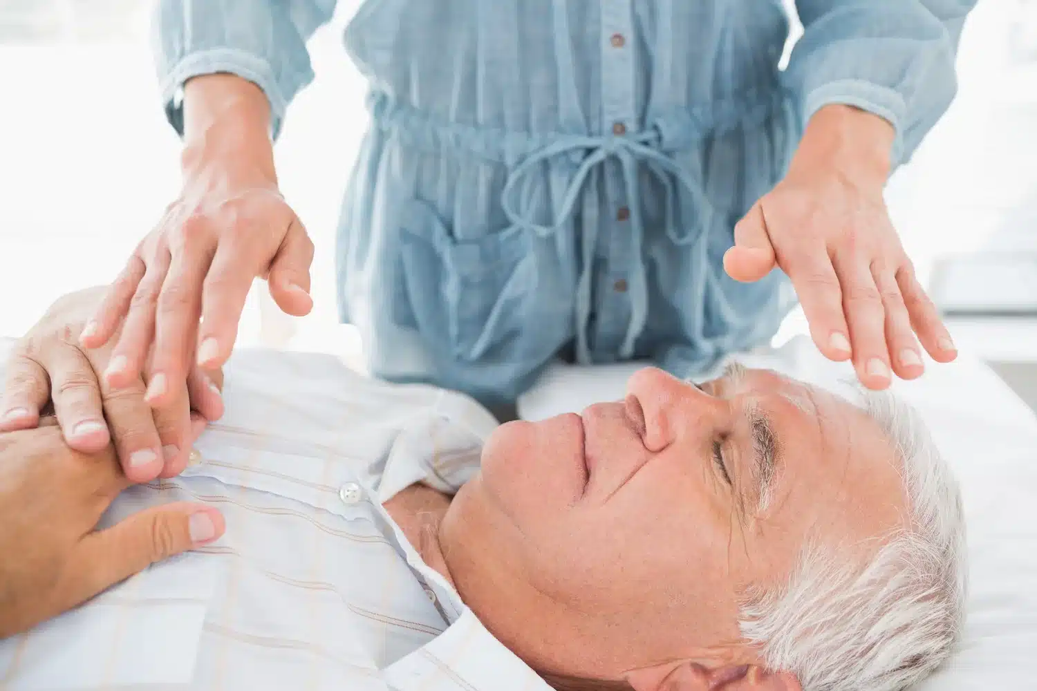 homme âgé allongé recevant un soin reiki avec les mains du praticien au-dessus de son visage